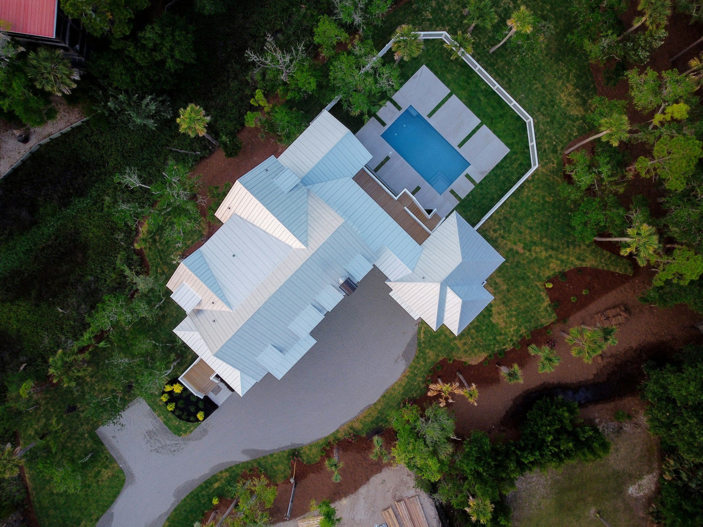 Drone view of a white standing-seam metal roof beside a pool