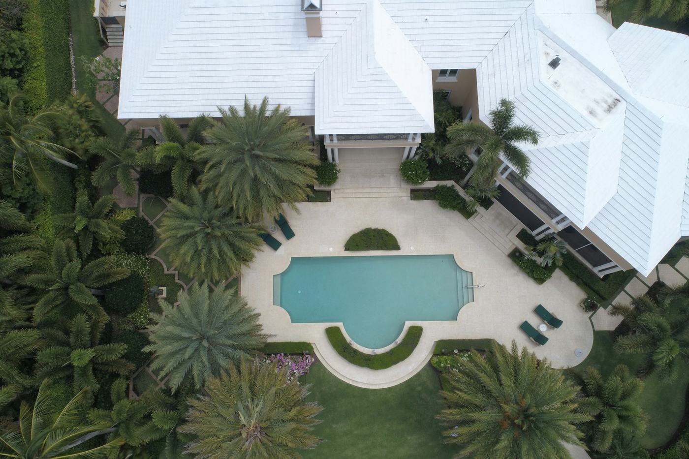 Drone view of white metal roofs, a pool and palms in Naples, Florida