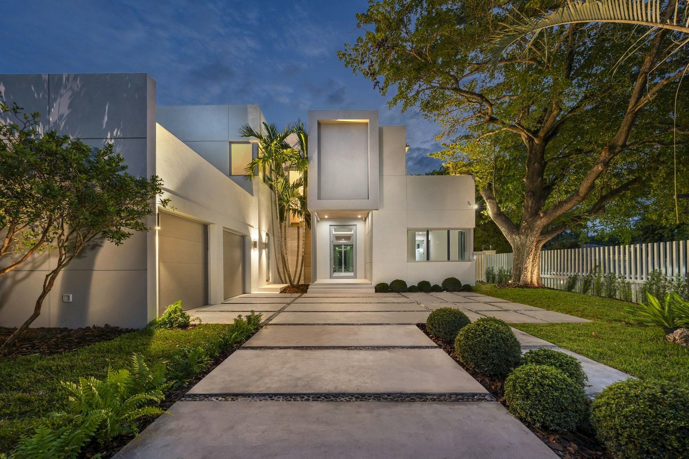 White contemporary South Florida home with a lit glass entry at twilight